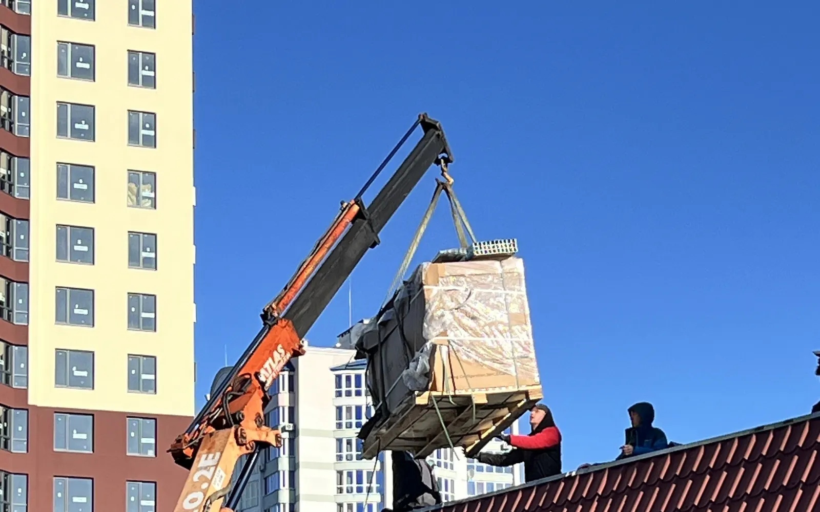 Підйом палети сонячних панелей краном на дах